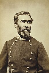 A man with salt-and-pepper hair, a mustache, and a full beard wearing a double-breasted military jacket