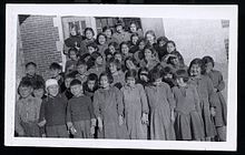 Group photo of Indigenous students in front of a brick building. A nun is visible in the back row.