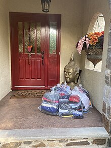 photograph of a group of folded clothes in bags, under a covered porch outside of a red door.