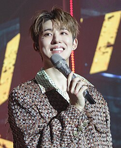 B.I holding a microphone and smiling at his first solo concert on December 10, 2022