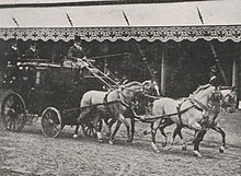 Photo en noir et blanc représentant une voiture tirée par quatre chevaux gris.