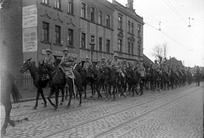 Photo noir et blanc d'une colonne de cavaliers portant le casque et remontant une rue.