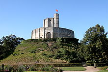 A small castle comprising a round keep surrounded by a tall encircling wall on top of a man-made hill