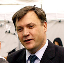 A man in his early 40s, with brown hair parted on the left, wearing a dark suit