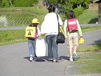 Two sisters wearing pink randoseru. One of them with a yellow plastic cover.