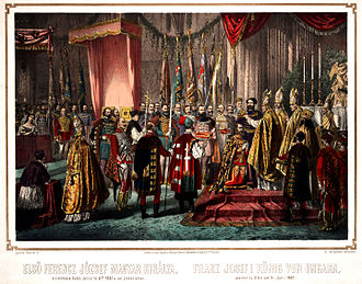 A bishop puts a crown on the head of a bearded man kneeling before him in a crowded large hall