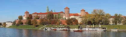 Castelo de Wawel visto do rio Vístula, Cracóvia, Polônia. O castelo real e a colina Wawel, no qual está situado, constituem o local de maior importância histórica e cultural da Polônia. Uma residência fortificada foi construída por ordem do rei Casimiro III, o Grande e ampliada ao longo dos séculos em várias estruturas ao redor de um pátio em estilo italiano. O castelo faz parte de um complexo arquitetônico fortificado erguido no topo de um afloramento de calcário. O complexo consiste em vários edifícios de grande importância histórica e nacional, incluindo a Catedral de Wawel, onde os monarcas poloneses foram coroados e enterrados. (definição 10 175 × 3 058)