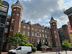 Color image looking up at red, brick building with staircase before the entrance and in between two towers