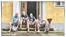 The band sitting on the stairs of a yellow house