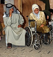 woman seated in a wheelchair with military personnel in background