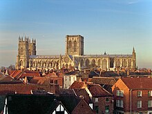 York Minster seen from the side - a long building with a pair of towers at one end and a massive central tower with two perpendicular windows. The round rose window can be seen on the south transcept.