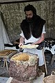 Photographie montrant un homme costumé debout, manipulant de la cire d'abeille.