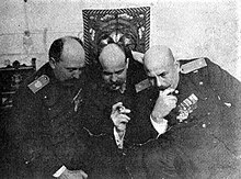 Černobílá fotografie tří mužů v důstojnických uniformách, kteří se soustředěně dívají kupředu dolů, snad na stůl před nimi, který však na fotografii není ukázán.