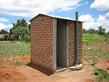 A small brick structure with four walls, an empty doorway, and a tall exhaust pipe.