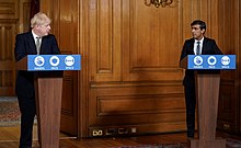 Prime Minister Boris Johnson delivers a press conference on 22 October 2020 with Chancellor of the Exchequer Rishi Sunak. The "Hands, Face, Space" slogan is displayed on their podiums Boris Johnson Covid-19 Presser (50516975857).jpg