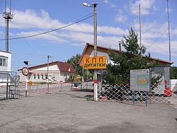 Three small buildings beside a road. The road is blocked with a white and red striped gate and a yellow and red sign reads "KPP Dityatki" in Ukrainian