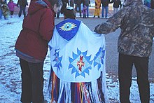 Una fotografia a colori di una giovane ragazza in uno scialle tradizionale tra due adulti