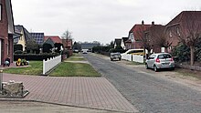 Kleine Straße mit Banketten, links und rechts Wohnhäuser mit Gärten