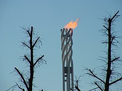 Flamme olympique au sommet d'une tour composé de quatre tubes qui forment une vrille au sommet.