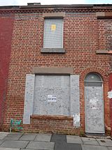 A colour photo of a red-bricked house with boarded up windows and doors