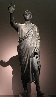 The Orator, c. 100 BCE, an Etrusco-Roman bronze sculpture depicting Aule Metele (Latin: Aulus Metellus), an Etruscan man wearing a Roman toga while engaged in rhetoric; the statue features an inscription in the Etruscan alphabet. Arringatore.jpg