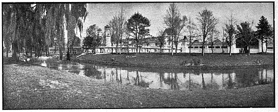 Building fronted by a curving river in front with trees and open park-like areas.