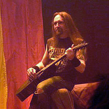 Guitarist Jed Simon sitting on the arm of a couch, playing guitar