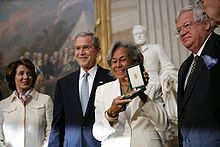 Черная женщина держит высоко награду, врученную президентом Джорджем Бушем и двумя другими высокопоставленными лицами