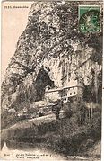 Carte postale ancienne avec un château au pied d'une montagne, au creux d'une grotte.