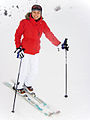 A female skier in winter clothes: jacket, hat, thick gloves, warm pants and ski boots