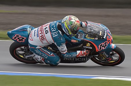 A motorcycle racer with an intricately decorated helmet leaning into the track during a race