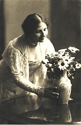 Ida Dehmel mirando y tocando un jarrón con flores. La imagen está en blanco y negro.