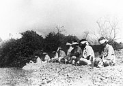 The Sikh prisoners are here seen seated blindfolded with target marks hanging over their hearts and stakes placed in the ground in front of them bearing the butt numbers of each "target". They sit with dignity awaiting their end.