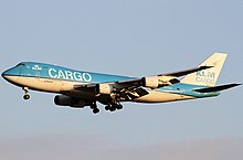 Large four-engine jet freighter whose body are painted in two blue and white halves; the top blue half has large lettering. The stabilizer is mostly white. It is on approach towards left of screen with landing gear extended