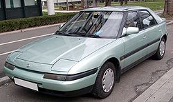 Un automóvil Mazda 323/protegé modelu 1994 nun aparcamientu públicu.