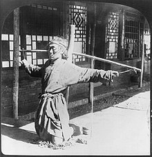 Prisoner kneeling on chains, thumbs supporting arms, photographic print on stereo card, Mukden, China (c. 1906) Punishment china 1900.jpg