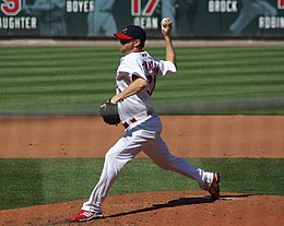 A man in a white baseball uniform pitches a ball from the mound