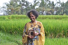 An upper body shot of woman standing in a grassy field. She is holding a copy of a novel and is smiling.