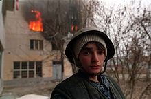 A Chechen stands near a burning house in Grozny. Evstafiev-chechnya-boy-house-burns.jpg