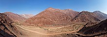 Une vallée encaissée, des montagnes arides à la roche striée de rouge, d'ocre et de brun, un train filant le long de canaux d'irrigation.