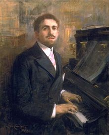 oil painting of a white man, sitting at a piano but looking towards the viewer. The man has neat brown hair, a moustache and neat beard.