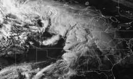 Grayscale satellite image of a large cluster of clouds arranged in a semi-coherent line from Texas northeastward to Wisconsin