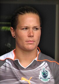 A head-and-shoulders photograph of Ashlyn Harris, a white woman in her mid-20s, dressed in a predominately grey soccer uniform with orange piping; she is looking to her left.