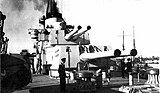 Vue d'une tourelle et de quatre canons sur un navire de guerre avec un homme debout à gauche, habillé en marin