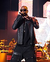 A man dressed in black rapping in front of a band