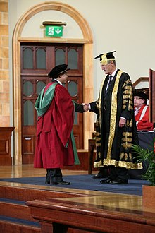 A new PhD graduate from the University of Birmingham, wearing a doctor's bonnet, shakes hands with the Chancellor. PhD graduand shaking hands with Sir Dominic Cadbury, the Chancellor of the University of Birmingham - 20120705.jpg