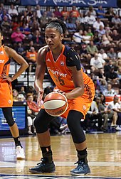 player with ball at the free throw line wearing orange uniform and black kinesiology tape, crowded stands visible behind her