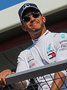 A black man in his early thirties with short facial hair smiling while wearing a hat.