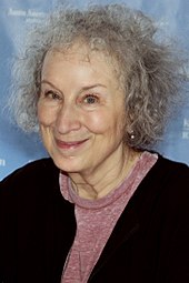 Elderly woman with grey hair wearing a black sweater and a pink shirt