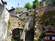 Photographie représentant le bas de la rue Chauchat construite en escaliers et collée contre une muraille de la quatrième enceinte.